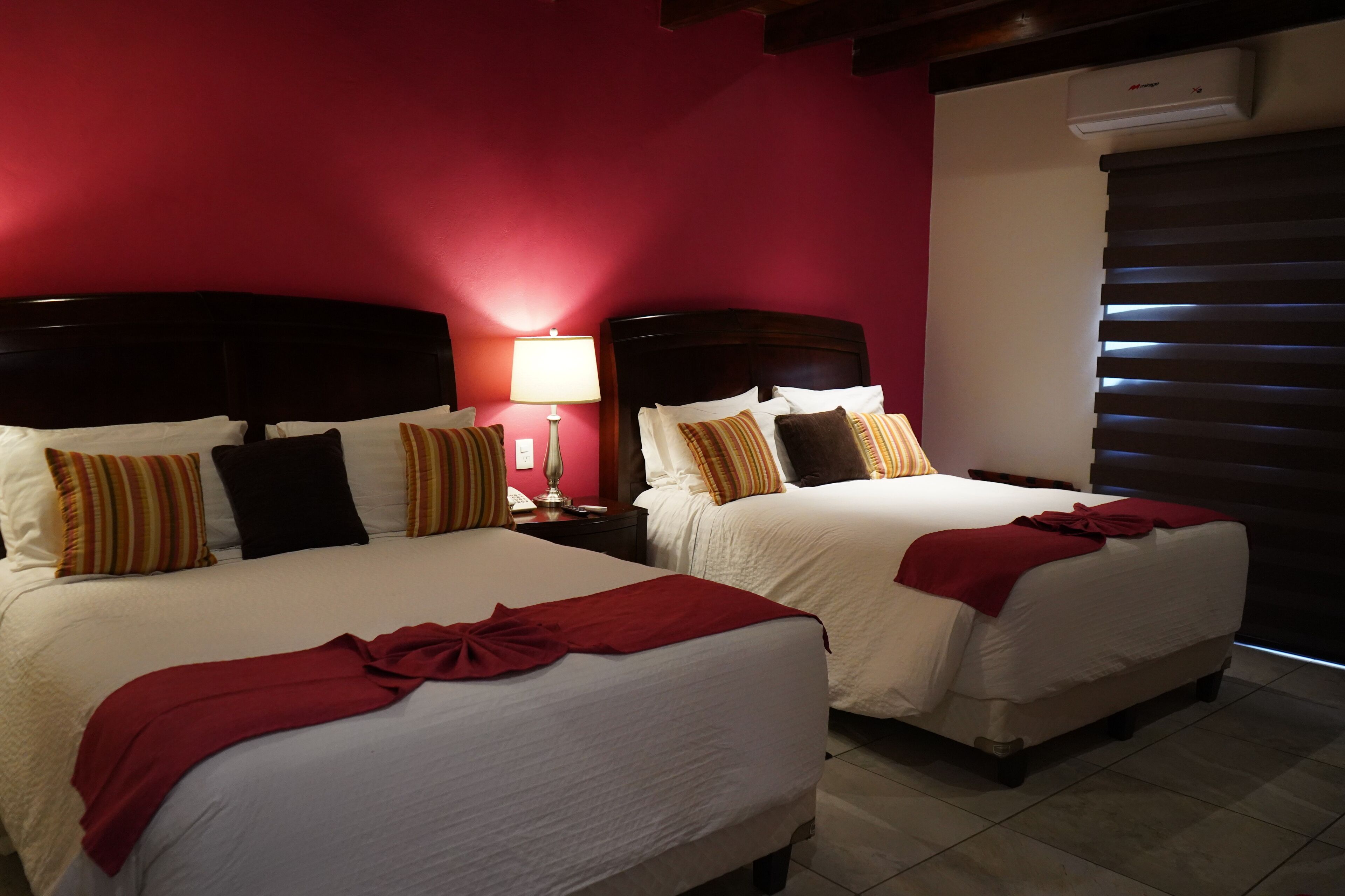 Habitación de hotel con dos camas, paredes rojas y una mesita de noche con lámpara.