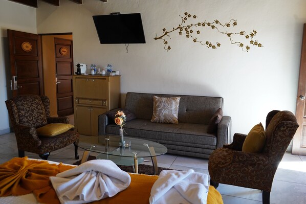 Una sala de estar con un sofá, dos sillones estampados, una mesa de centro y un televisor de pantalla plana montado en la pared.