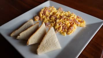 A white plate with scrambled eggs and ham, accompanied by three slices of toast on a wooden table.