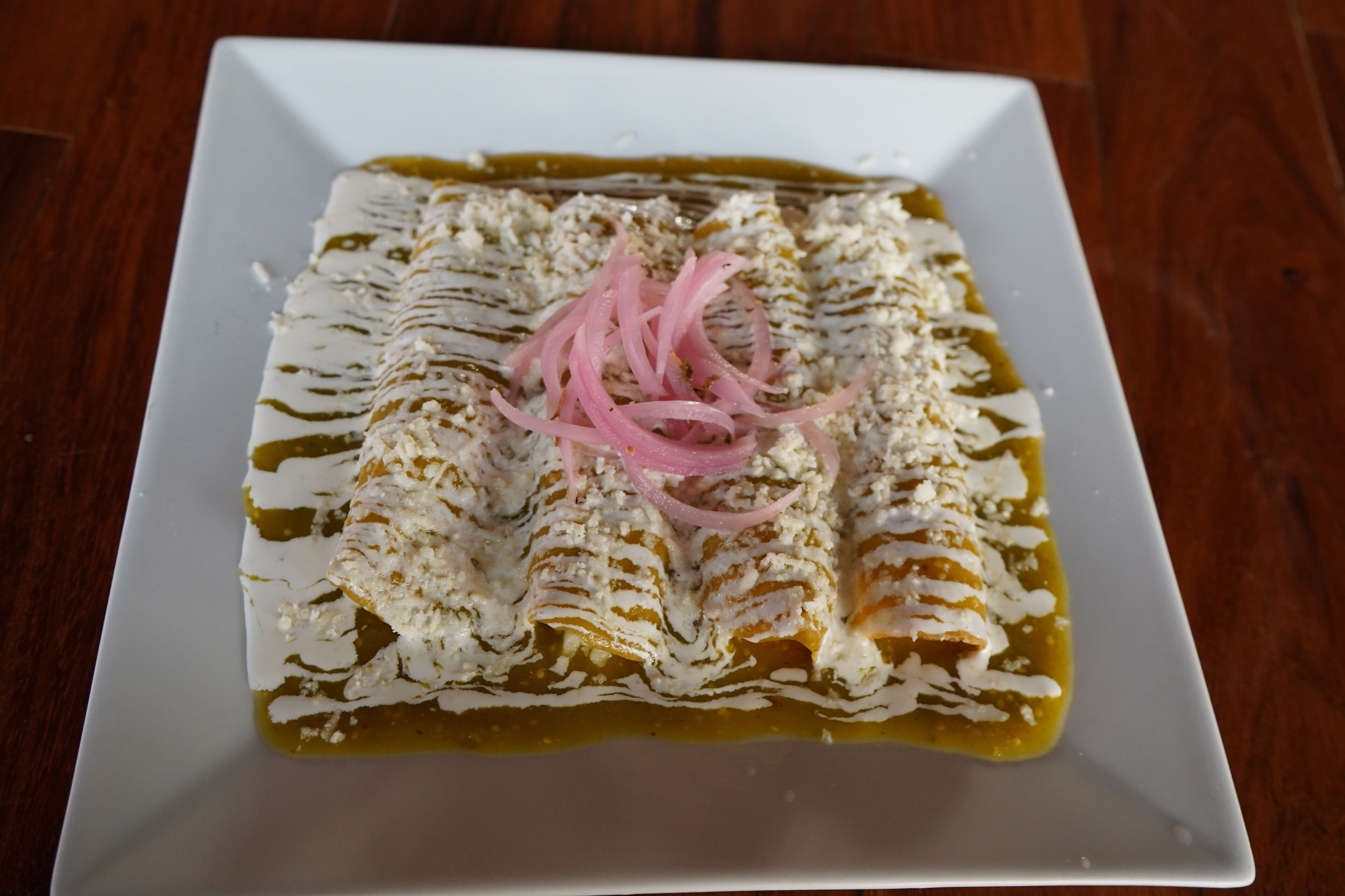 A plate of enchiladas with a white sauce, cheese, and pink onion garnish on a white plate.