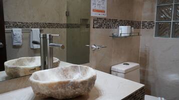 A bathroom with a stone basin, a toilet, and a shower area.