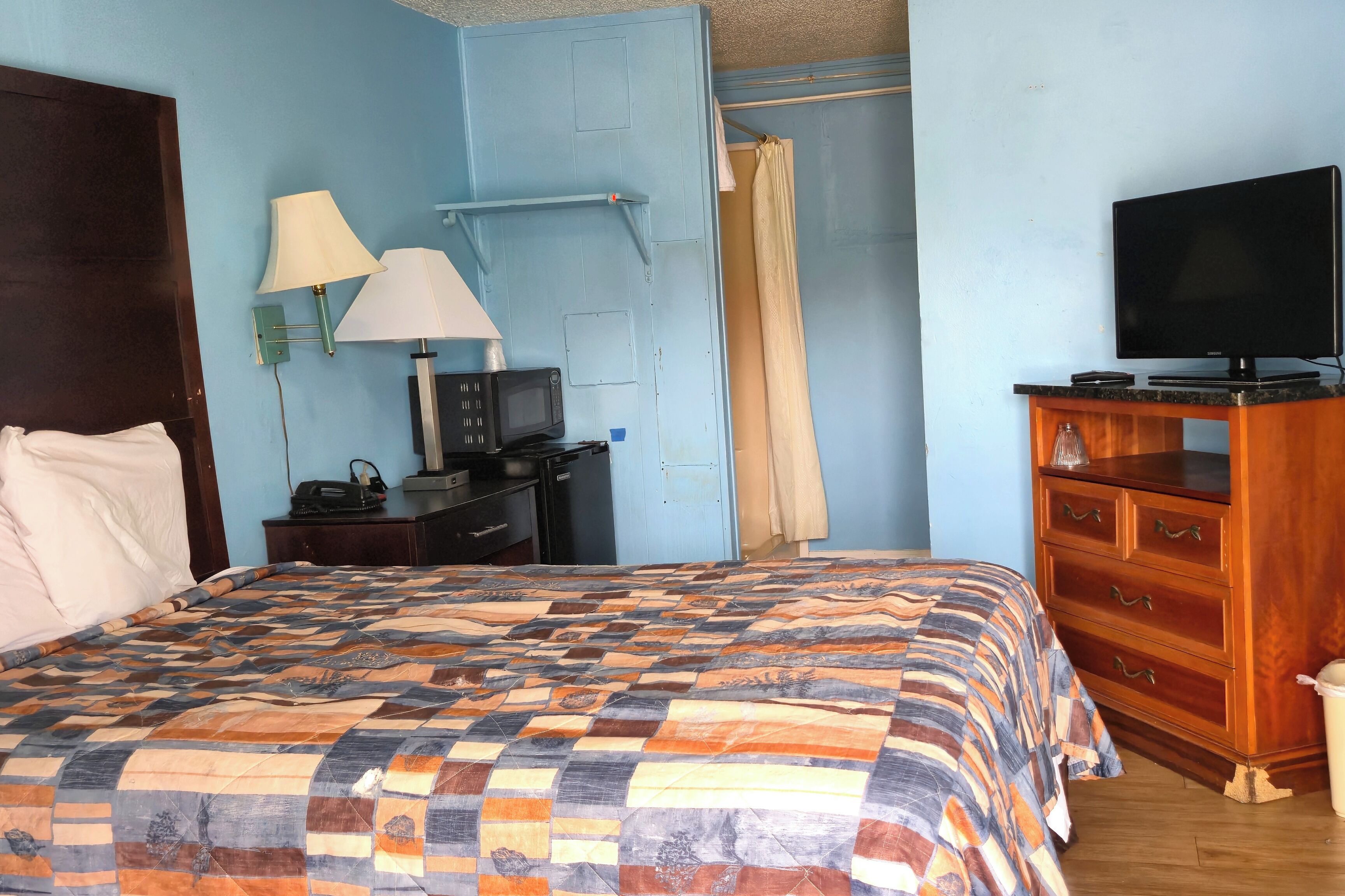 A bedroom with a large bed, a wooden dresser, a television, a desk with a lamp, and a shower curtain.