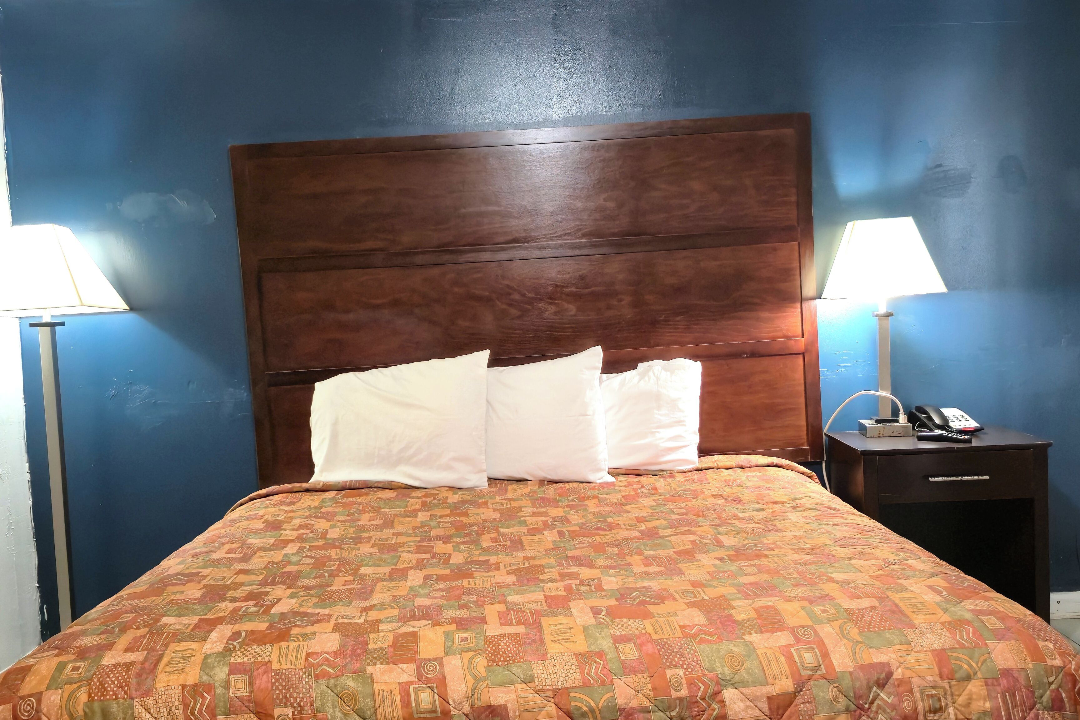 A hotel room with a large bed, two bedside tables, and a nightstand with a lamp and phone.
