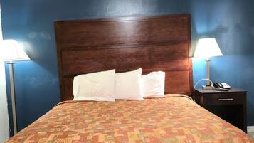 A hotel room with a large bed, two bedside tables, and a nightstand with a lamp and phone.