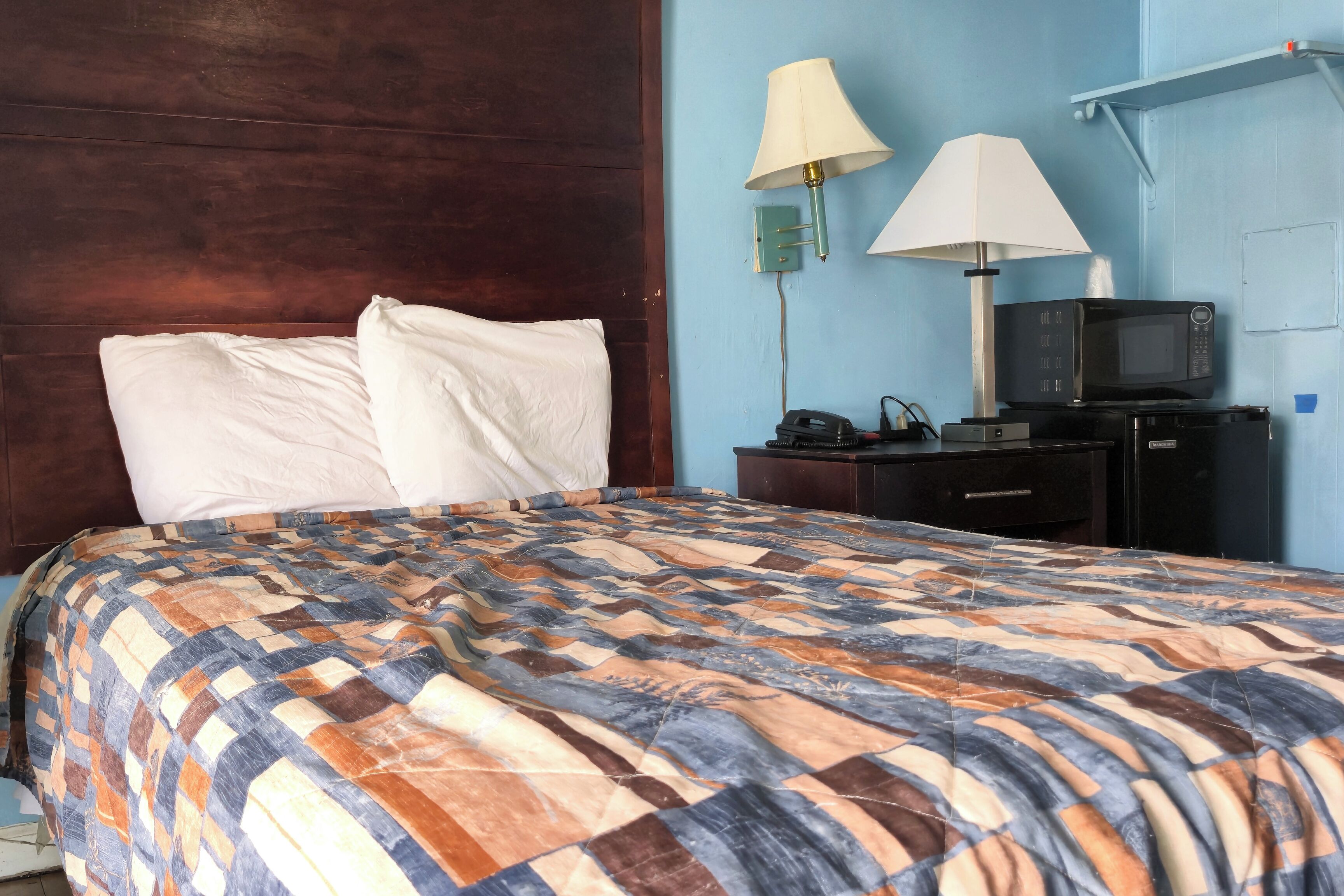A hotel room with a bed, two wall-mounted lamps, a microwave, and a small table.
