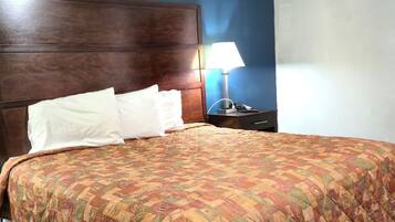 Una cama bien hecha con una colcha estampada, un cabecero de madera y una mesita de noche con una lámpara.