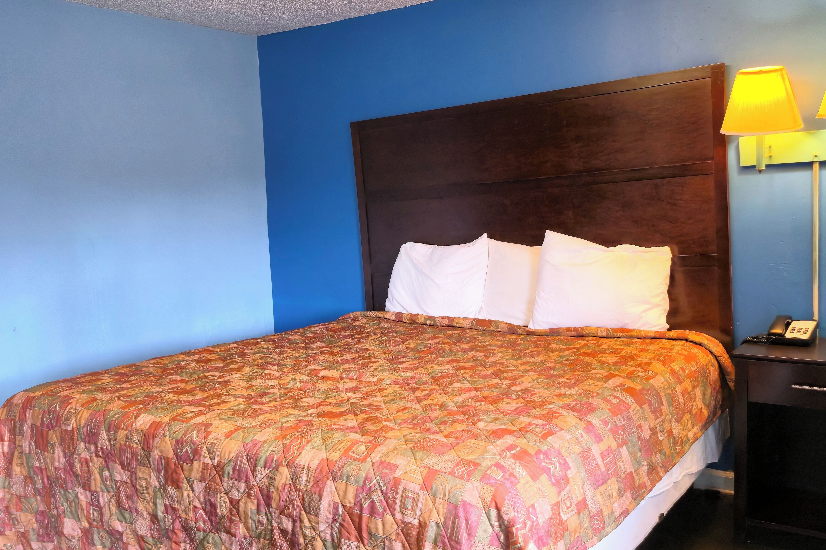 A hotel room with a large bed, a wooden headboard, a nightstand with a lamp, and a phone.