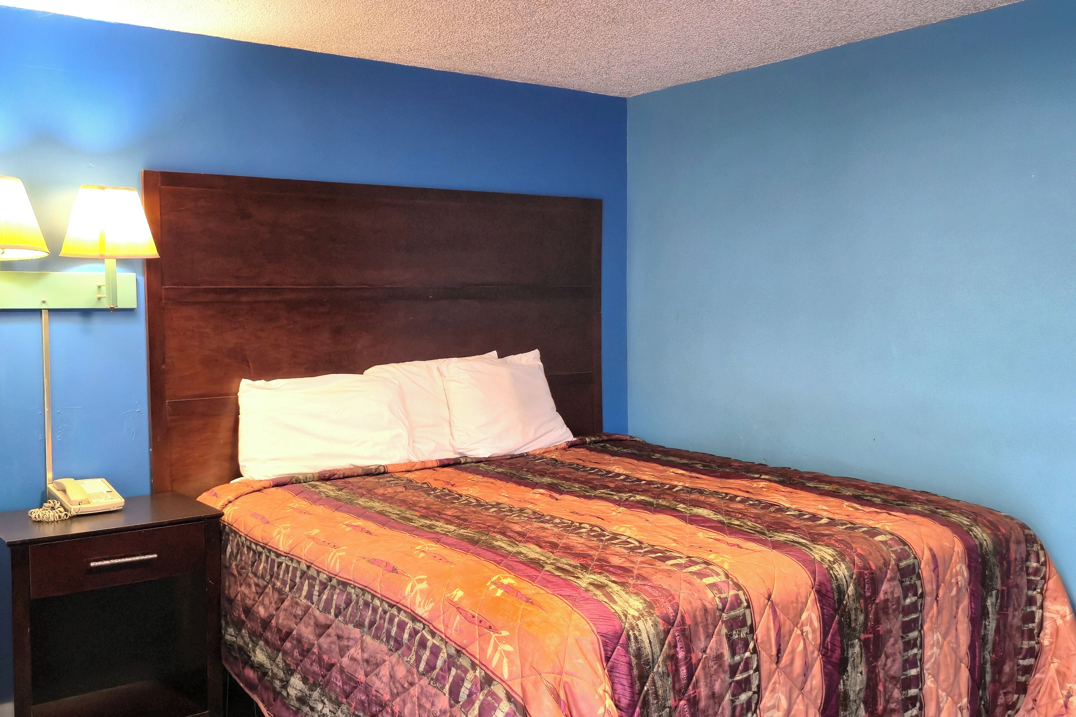 A hotel room with a large bed, a nightstand with a lamp, and a blue wall.