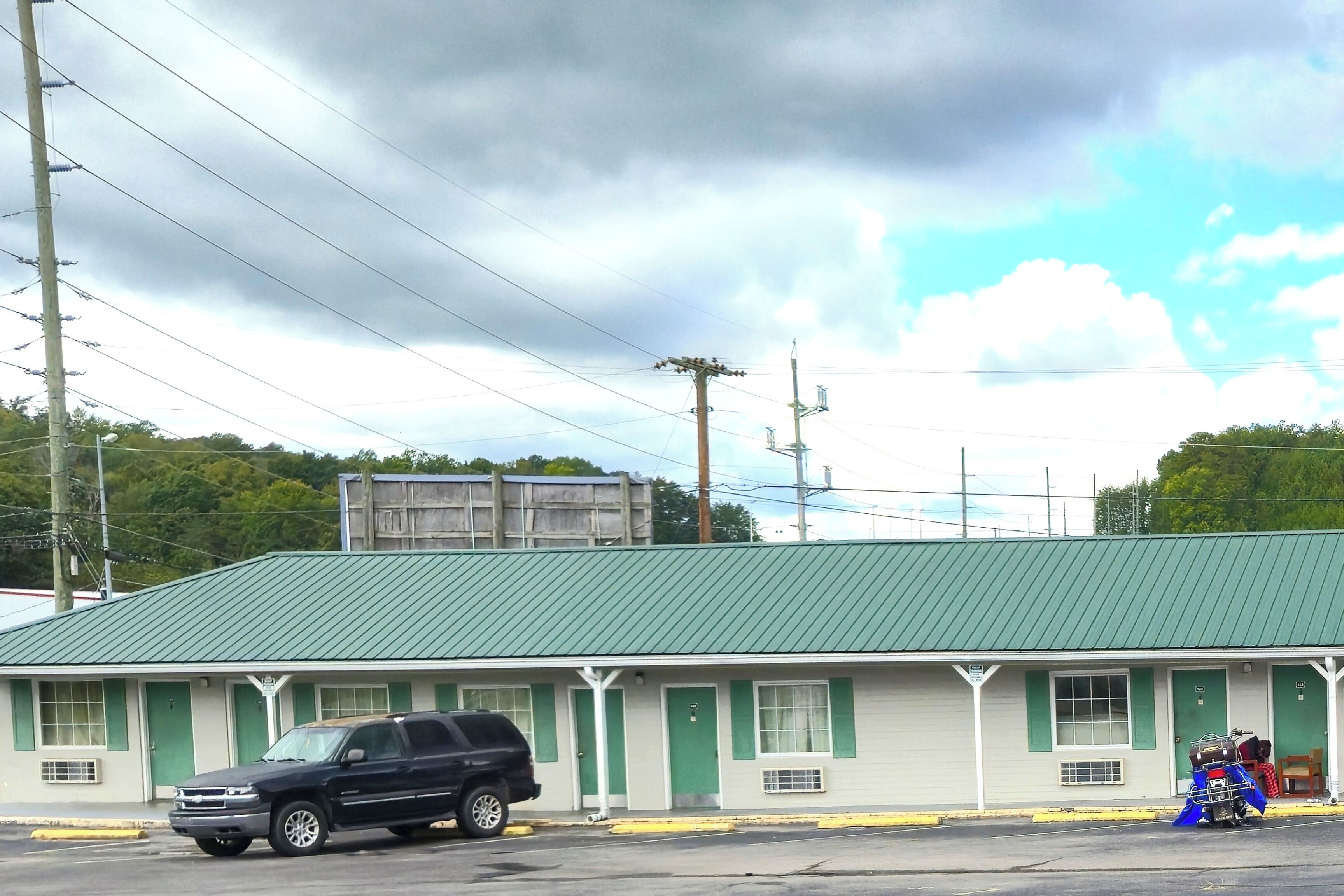 A motel with a green roof and white walls, featuring a row of rooms with green doors and windows.
