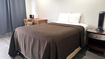 A hotel room with a bed, a bedside table, a chair, a desk, and a heater.