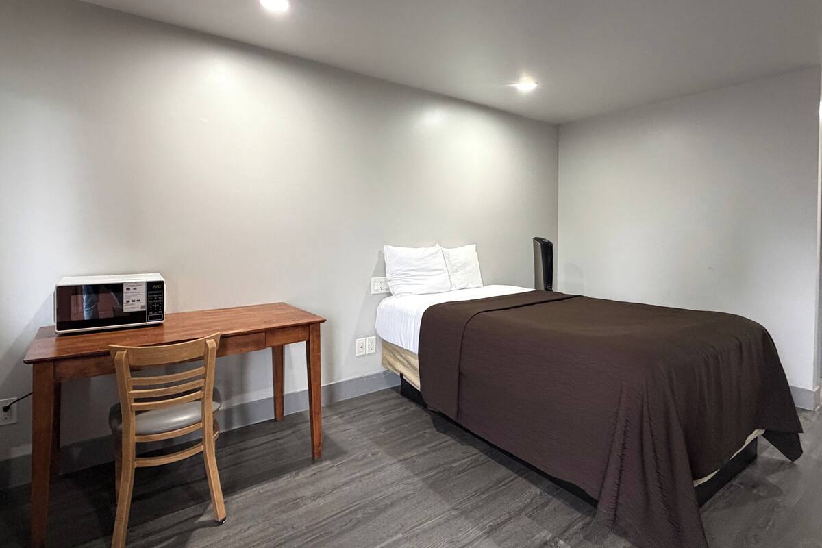 A bedroom with a bed, a wooden desk, a chair, and a microwave.