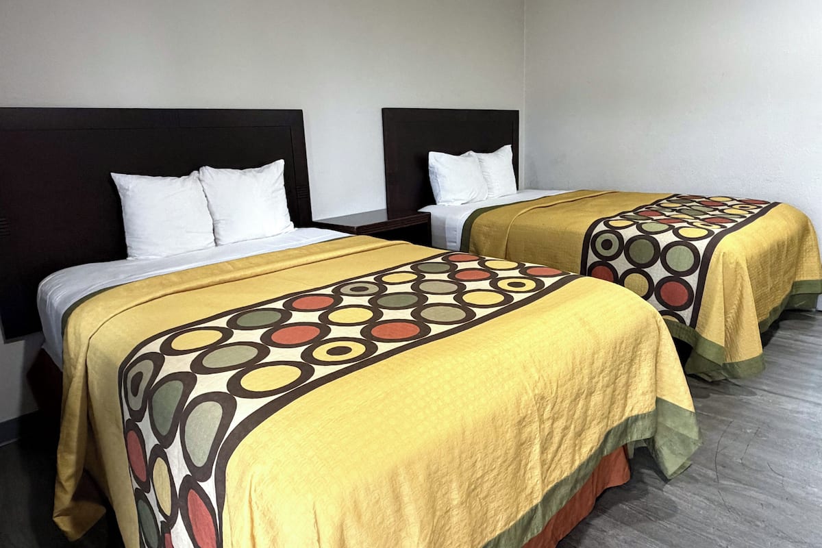 Two single beds with headboards, white pillows, and yellow bedspreads with a circular pattern.