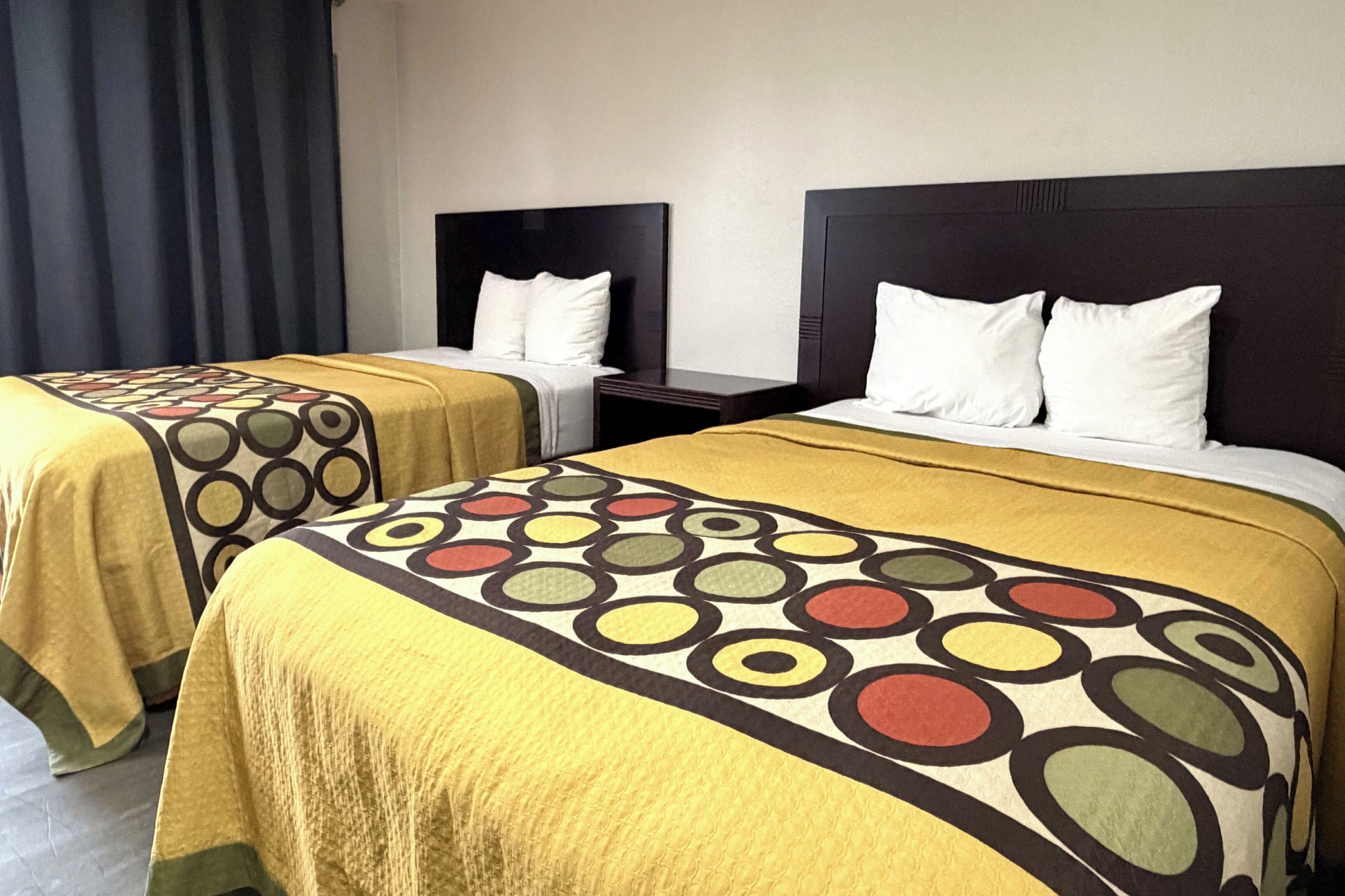 Two twin beds with matching headboards and footboards, each with a white pillow and a yellow bedspread with a circular pattern.