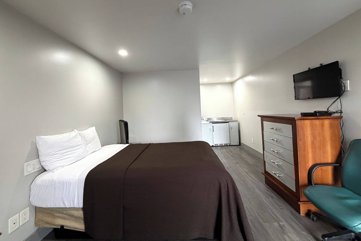 A hotel room with a bed, a desk, a chair, a TV, and a dresser.