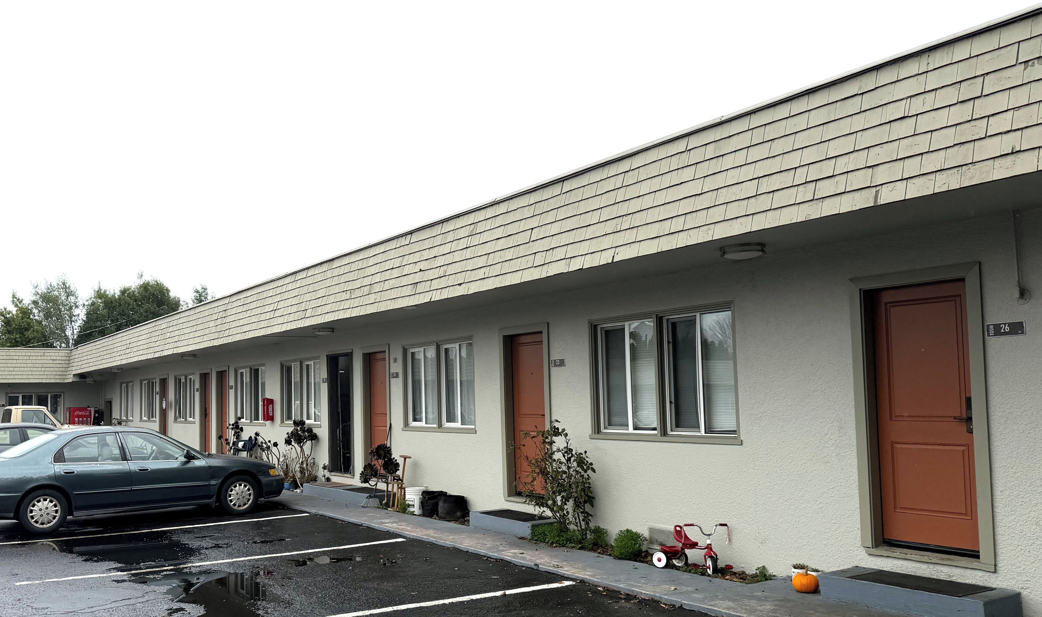 Un motel amb una filera d'habitacions, cadascuna amb una porta i una finestra. Hi ha un cotxe estacionat al davant, i una testuda i un petit cotxe de joguina vermell a la vorera.