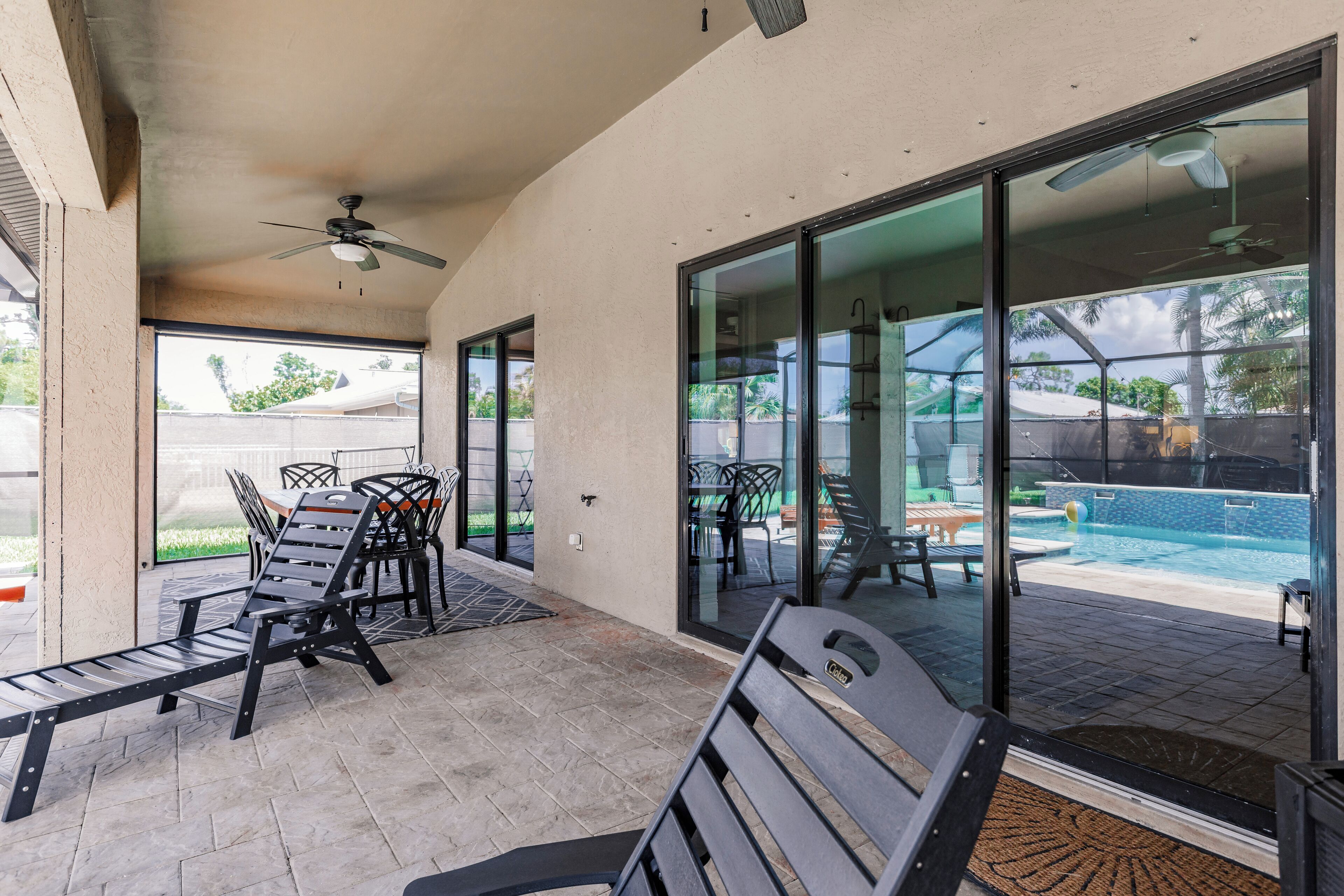 A covered patio area with outdoor furniture, a pool, and a glass door leading to a poolside area.