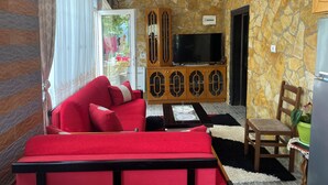 A living room with a red sofa, a wooden cabinet with a TV, and a stone wall. - Vila across Tepelena (Tepelenë)