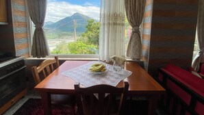 A dining area with a table set for two, a view of a mountain, and a kitchen with a stove. - Vila across Tepelena (Tepelenë)