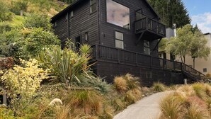 A modern black house with a balcony, surrounded by lush greenery and a winding path.