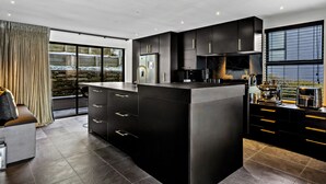 A modern kitchen with a central island, black cabinetry, and a view of a snowy outdoor area through large windows.