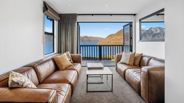 A modern living room with leather sofas, a coffee table, and large windows offering a mountain view.