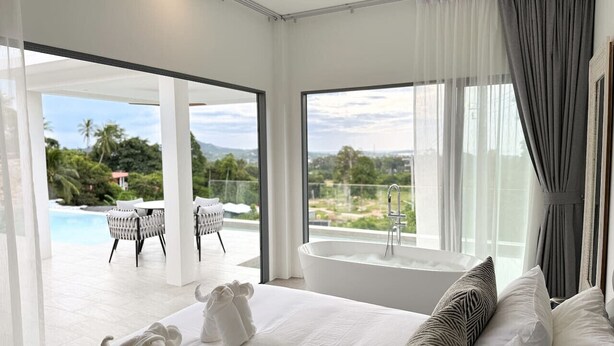 Une chambre d’hôtel moderne dotée d’un grand lit, d’une baignoire et offrant une vue sur une piscine et un espace verdoyant.