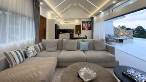 Un salon moderne avec un grand canapé d’angle, une table basse et un coin repas à l’arrière-plan.
