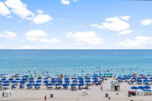 A beach with numerous umbrellas and sun loungers, a lifeguard tower, and a clear view of the ocean. - Sunset Views, Beachfront & Resort Pools (Panama City Beach)