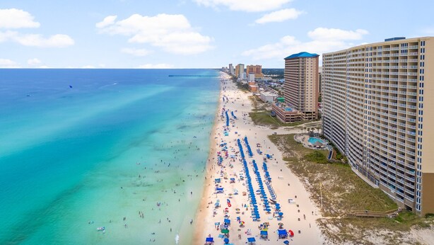 A coastal hotel with a beach view, multiple balconies, and a pier in the background.