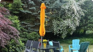 A patio with a glass table and chairs, an orange umbrella, and a small flower arrangement.