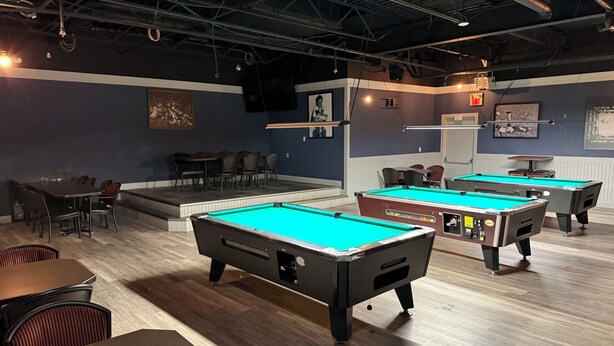 Eine Poolhalle mit mehreren Billardtischen, Sitzgelegenheiten und einer Bühne.