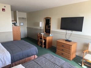 A hotel room with two beds, a desk with a chair, a dresser, a television, and a mirror.