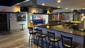 Eine Bar mit Hockstühlen, einer Theke, Spielautomaten und einer Wanduhr.