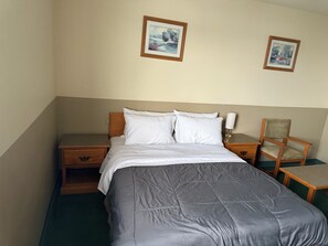 A neatly made bed with white linens, a wooden nightstand with a lamp, and a chair.
