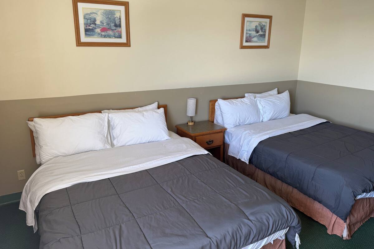 A hotel room with two beds, a nightstand, and two framed pictures on the wall.