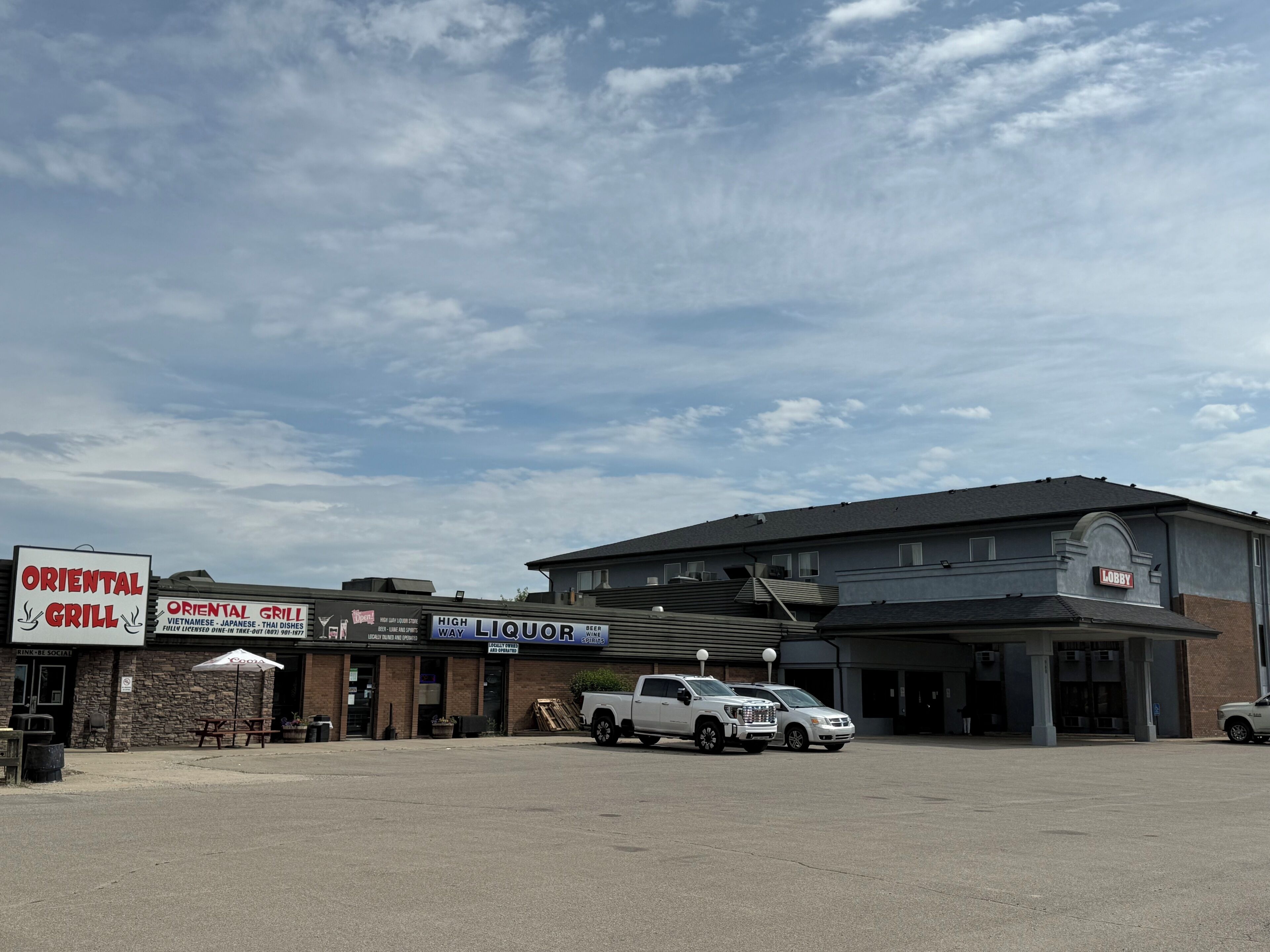 A building with a sign for 'Oriental Grill' and 'High Liquor' on the ground floor, a parking lot, and a 'Lobby' sign on the building.