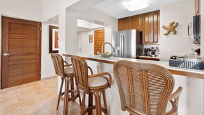 A modern kitchen with wooden cabinets, a stainless steel refrigerator, and a bar area with wicker chairs. - 3-bedroom apartment in perfect Palmas del Mar with pool and beach access (Palmas del Mar)
