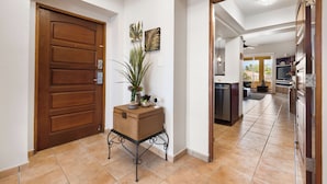 A hallway with a wooden door, a wicker basket with plants, and a view into a living area with a kitchen. - 3-bedroom apartment in perfect Palmas del Mar with pool and beach access (Palmas del Mar)