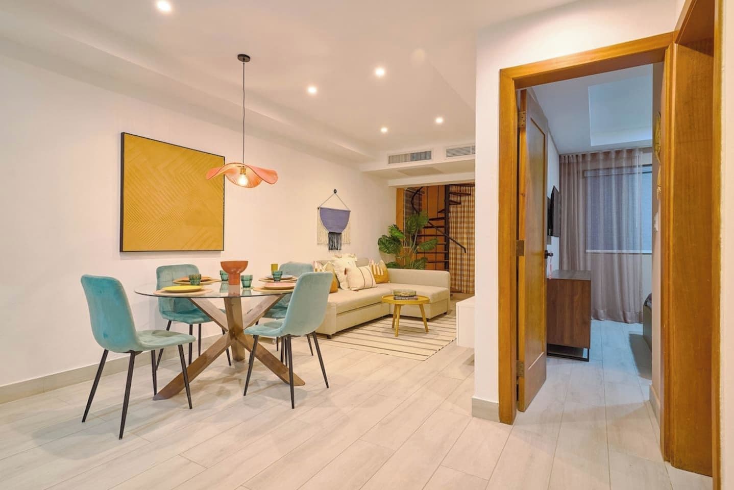 A modern living room with a dining area, a sofa, a coffee table, and a hanging light fixture.