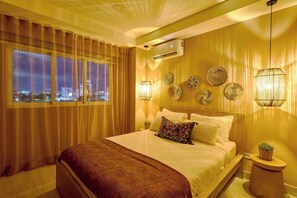 Habitación de hotel con una cama grande, cortinas, vistas a la ciudad, aire acondicionado empotrado y paneles decorativos en la pared.