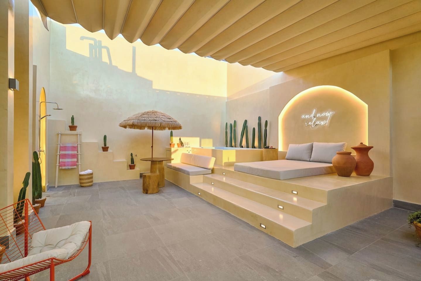 A modern interior with a seating area, a table with a thatched umbrella, and a wall with a neon sign.