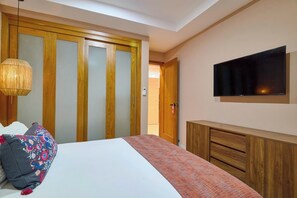 A bedroom with a bed, a television mounted on the wall, a wardrobe with a mirror, and a door leading to another room.