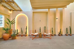 A spacious indoor area with a modern design, featuring a seating area with two orange chairs, several potted cacti, and a large illuminated wall.