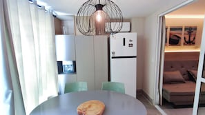 A compact living space with a dining table, chairs, a coffee machine, a refrigerator, and a sofa.