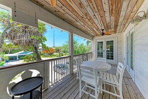 A covered porch with a ceiling fan, white outdoor furniture, and a view of a residential area. - Paradise on Pine (Anna Maria)
