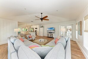 A spacious living room with a large grey sofa, a ceiling fan, and a television. - Paradise on Pine (Anna Maria)