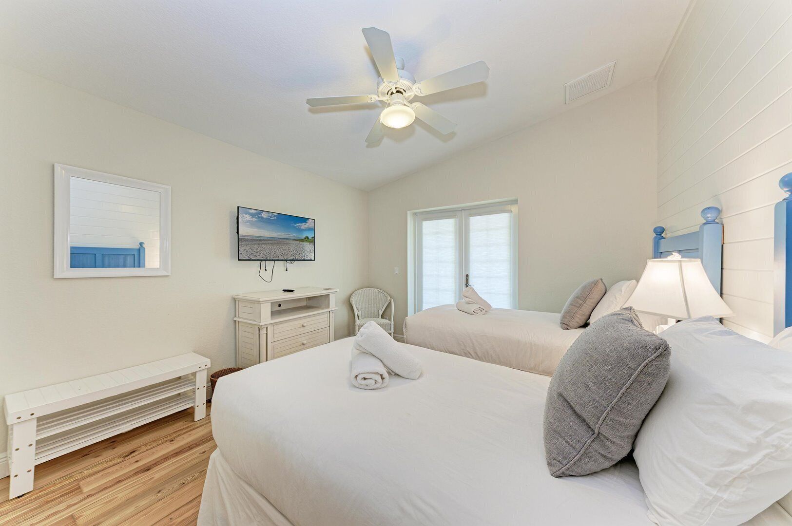 A hotel room with two beds, a ceiling fan, a TV, a window, and a white dresser.