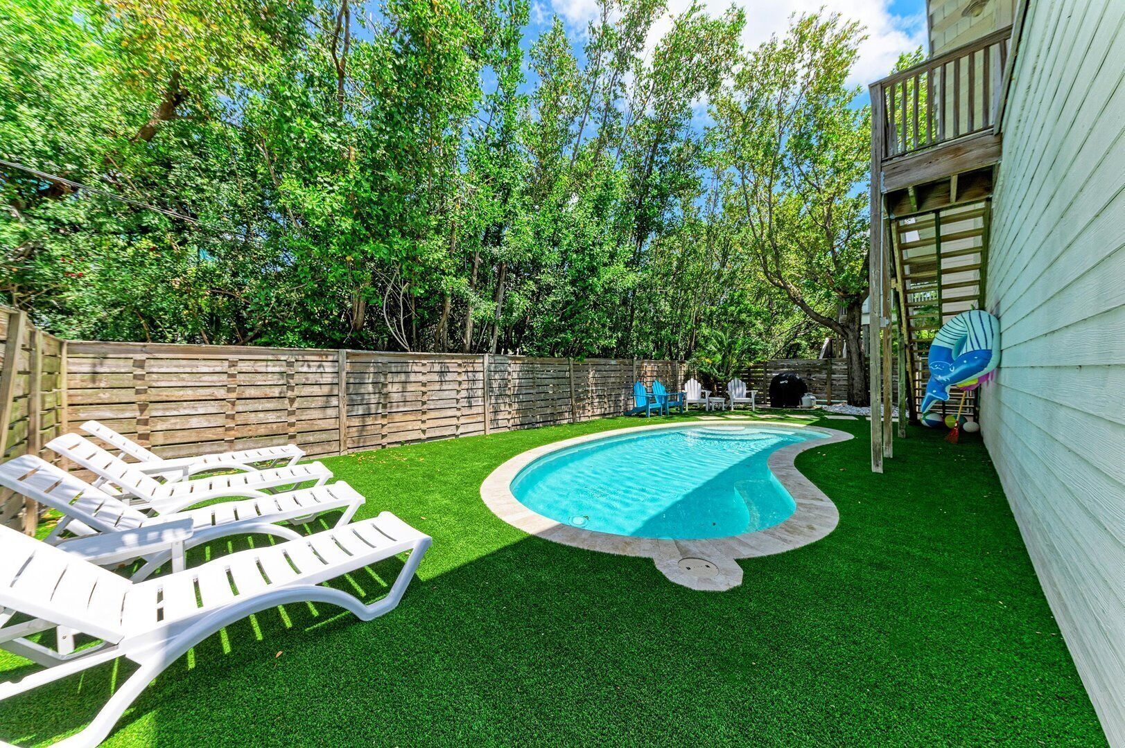 Ein Garten mit Schwimmbecken, Kunstrasen und einer Holzterrasse.