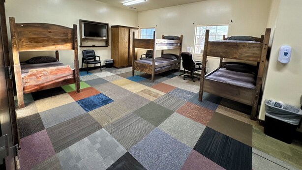A dormitory room with bunk beds, a desk, a chair, a TV, and a window. - Utah Prep Basecamp (Hurricane)