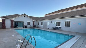 A swimming pool with a metal ladder, a covered patio area, and a building with a tiled roof and windows. - Utah Prep Basecamp (Hurricane)